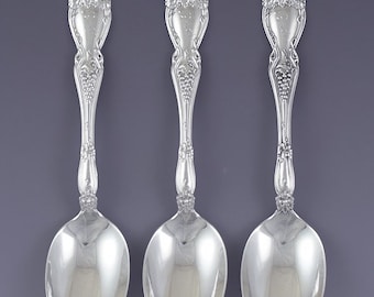 May include: Three silver spoons with ornate handles featuring a grapevine design. The spoons have a polished finish and are arranged in a row.