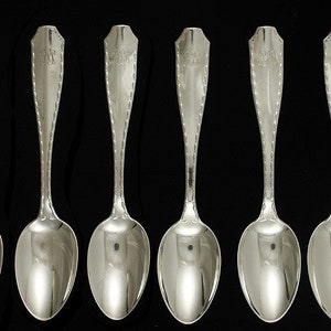 Puede incluir: Juego de seis cucharaditas de plata con mangos adornados. Las cucharas tienen un acabado pulido y están dispuestas en fila.