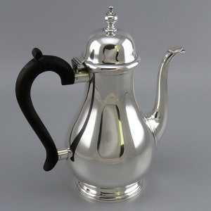 Może przedstawiać: Srebrny dzbanek do kawy z czarnym drewnianym uchwytem i kopułową pokrywką. Dzbanek ma kształt gruszki i zaokrąglony dzióbek.