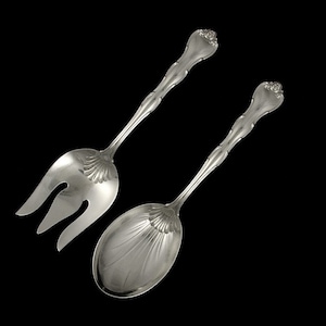 May include: A silver serving set with a fork and spoon. The fork has three tines and the spoon has a rounded bowl. Both pieces have ornate handles.