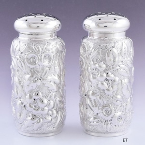 Puede incluir: Un par de saleros y pimenteros de plata con un diseño floral.