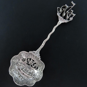 May include: A silver sugar spoon with a detailed design of a ship on the handle and a cutout design of a ship on the bowl.