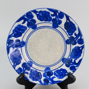 May include: A white ceramic plate with a blue floral design. The plate has a crackled glaze and a raised rim.