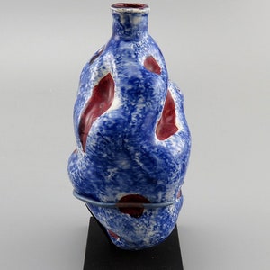 May include: A blue and red ceramic vase with an abstract, organic shape. The vase is on a black stand.