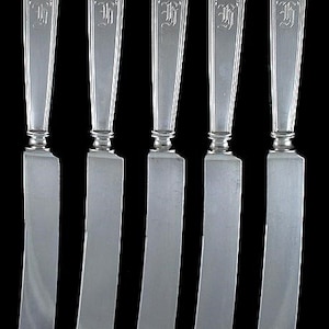 May include: Set of five silver butter knives with ornate handles and a monogrammed "H".