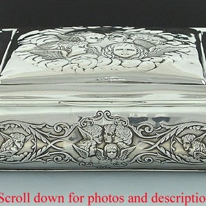 May include: A silver hinged box with an ornate design featuring cherubs and floral motifs. The lid is embossed with a scene of angels.