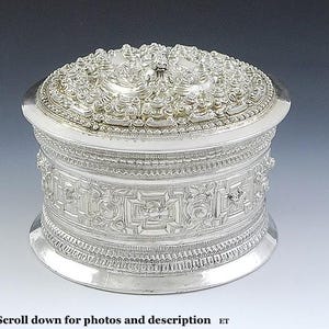 Puede incluir: Una caja redonda de plata con intrincados diseños florales y geométricos. La tapa está adornada con un motivo floral en relieve.