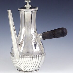 May include: A silver coffee pot with a wooden handle. The pot has a fluted design and a lid with a finial.