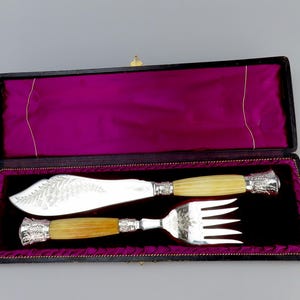 Puede incluir: Un juego de cuchillo y tenedor de mantequilla de plata con mangos de hueso en una caja forrada de terciopelo negro.