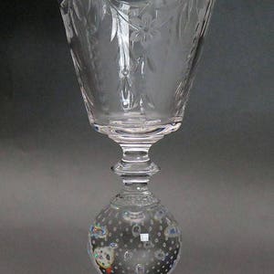 May include: A clear glass goblet with a wide, flared bowl and a decorative, etched design. The goblet has a round, textured base.