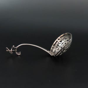 Può includere: Un cucchiaino da zucchero in argento con una ciotola decorata e traforata e un manico decorativo a forma di ramo stilizzato.