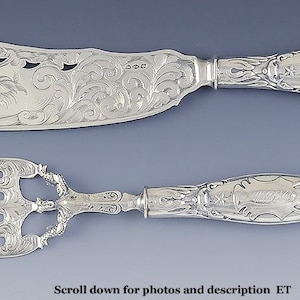 May include: A silver serving set with a knife and fork. Both pieces have ornate handles with engraved designs.