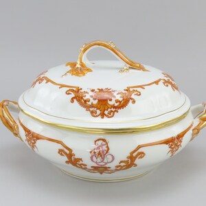 Może przedstawiać: Biała porcelanowa zupa z pokrywką, ozdobiona złotą obwódką i misternymi pomarańczowymi wzorami kwiatowymi. Zupa ma dwa uchwyty i złoty guzik na pokrywce.