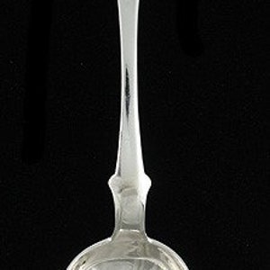May include: A silver spoon with an ornate handle and a rounded bowl. The handle is engraved with the initials "E.M.C."