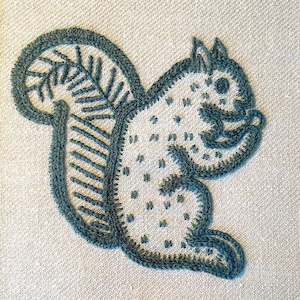May include: A green embroidered squirrel design on a beige fabric background.