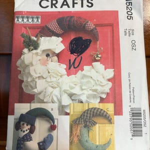 May include: A McCall's Crafts pattern packet featuring holiday craft designs. The packet includes images of a Santa Claus wreath, a snowman moon, and a crescent moon decoration. The packet is red and white with the text "MCCALL'S CRAFTS".