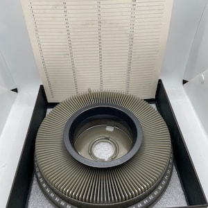 May include: A black Kodak slide carousel with a gray plastic disc that holds 120 slides. The disc is numbered from 1 to 120. The carousel is in a black box with a white foam lining.