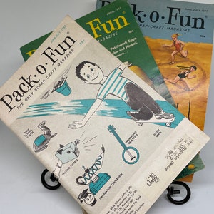 May include: Three vintage issues of Pack-o-Fun magazine, a scrap-craft magazine. The covers feature illustrations of children engaged in various activities, including a boy on a scooter, a girl playing with a bucket and shovel, and a girl playing with a doll. The magazine titles are printed in green and white, and the dates are printed in black.