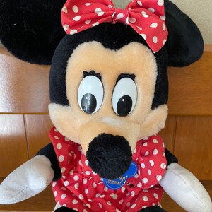 Pu&ograve; includere: Un giocattolo di peluche di Minnie Mouse, la fidanzata di Topolino. Indossa un vestito rosso con pois bianchi e un fiocco rosso con pois bianchi. Ha un naso nero e grandi occhi bianchi. Il giocattolo ha un'etichetta blu che dice "Disney's Original".
