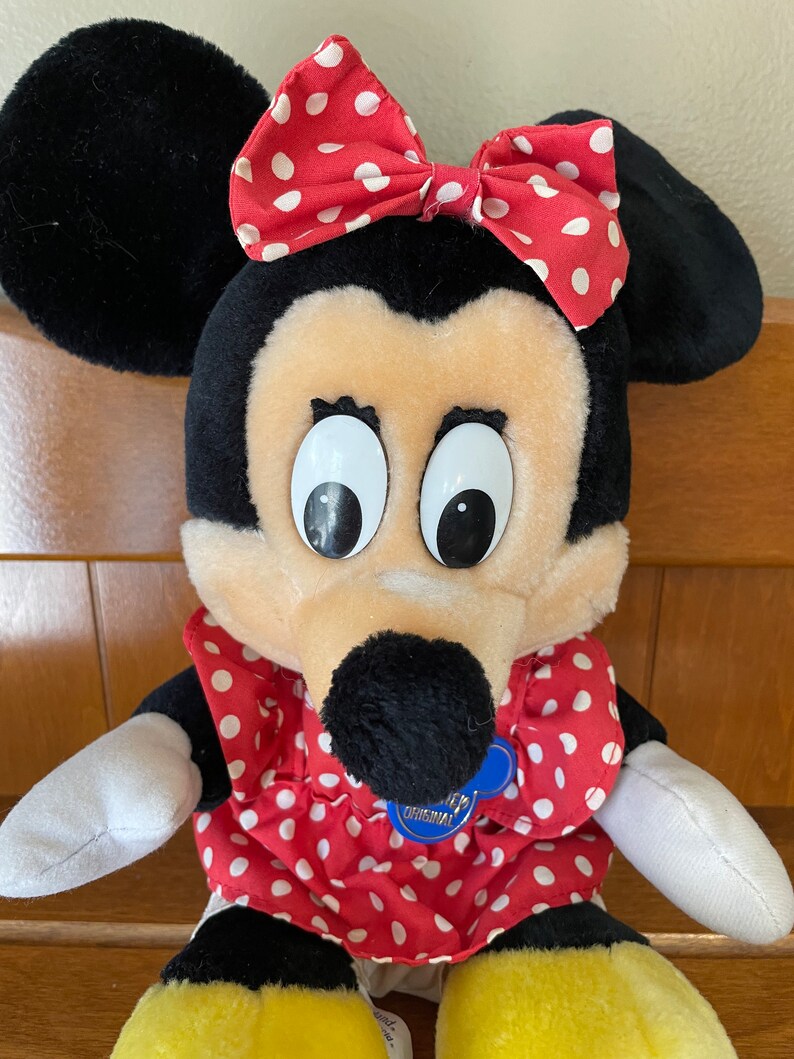 Pu&ograve; includere: Un giocattolo di peluche di Minnie Mouse, la fidanzata di Topolino. Indossa un vestito rosso con pois bianchi e un fiocco rosso con pois bianchi. Ha un naso nero e grandi occhi bianchi. Il giocattolo ha un'etichetta blu che dice "Disney's Original".