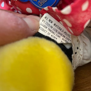 Pu&ograve; includere: Una bambola di stoffa a pois rossi e bianchi con una testa gialla e occhi neri. La bambola indossa un colletto di pizzo bianco e un'etichetta blu Disney Original attaccata al colletto. L'etichetta recita "ALL NEW MATERIALS-POLYES. ME 1525:PA 1378: OHIO PA 1378: CANASA TRADING CORP. BURBA RODUCT OF KOREA."