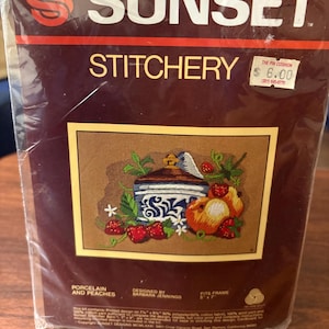 May include: A Sunset Stitchery kit for a pin cushion. The kit features a design of porcelain and peaches. The image shows a brown background with a blue and white porcelain jar, peaches, and strawberries. The kit fits a 5" x 7" frame.