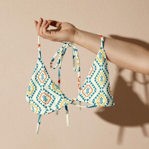 May include: A white bikini top with a geometric pattern in shades of blue, yellow, and red. The top has adjustable straps and a tie closure.