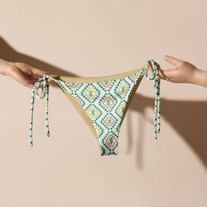 May include: A white bikini bottom with a geometric pattern in shades of blue, yellow, and orange. The bikini bottom has tie strings on both sides.