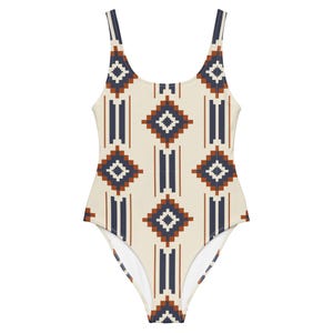 May include: A white one-piece swimsuit with a geometric pattern in shades of blue and brown. The pattern features repeating diamonds and vertical stripes.
