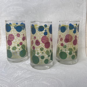May include: Set of three clear glass drinking glasses with a yellow, green, blue, and pink geometric pattern. The pattern features circles and a net-like design.
