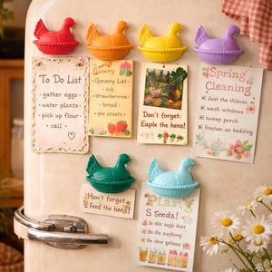 May include: A selection of fridge magnets shaped like chickens in red, orange, yellow, and purple. The magnets are holding notes with reminders, including a to-do list, a grocery list, and spring cleaning tasks.