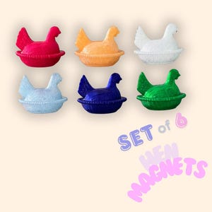 May include: A set of six hen magnets in red, orange, white, light blue, dark blue, and green. Each hen is in a nest-shaped base. The image includes the text "SET of 6 HEN MAGNETS".