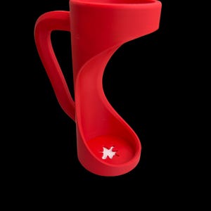 May include: A vibrant red mug with a unique, curved design. The handle is integrated into the body, and the base features a white, star-shaped detail. The mug is set against a black background, highlighting its modern aesthetic.