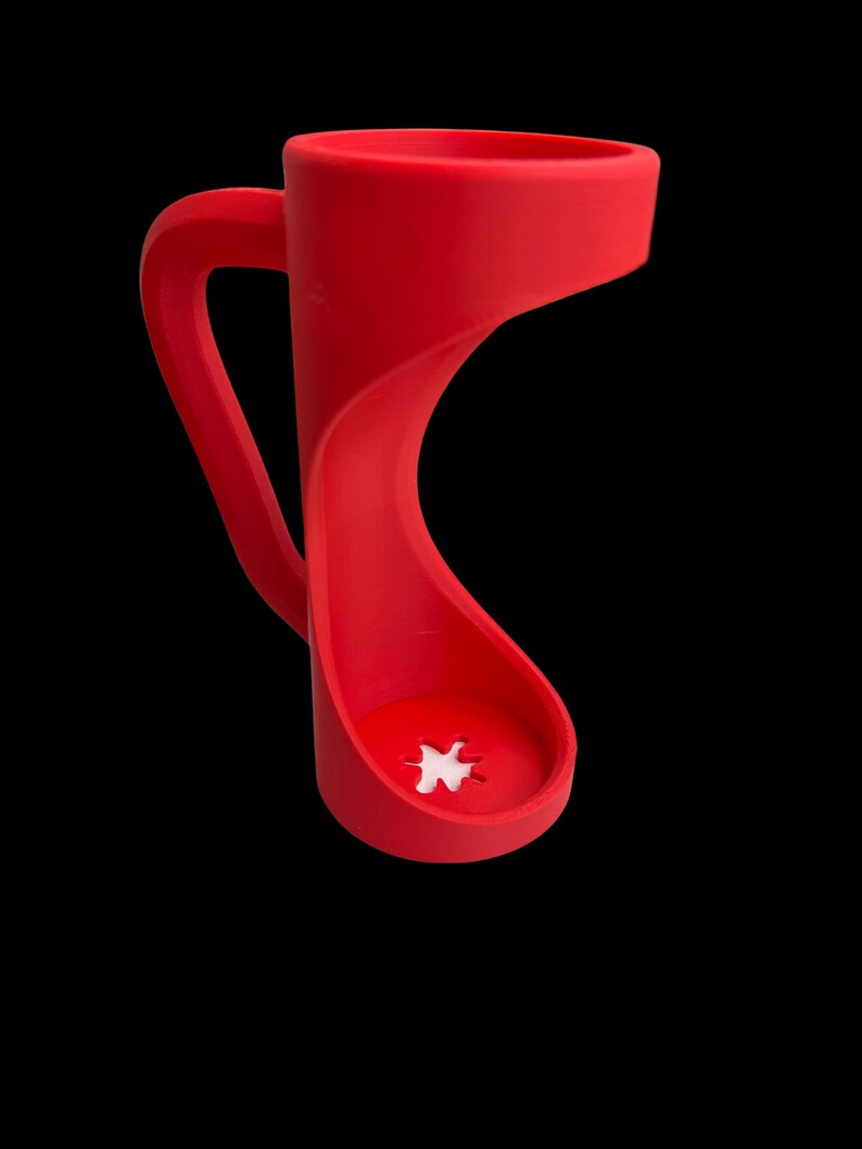 May include: A vibrant red mug with a unique, curved design. The handle is integrated into the body, and the base features a white, star-shaped detail. The mug is set against a black background, highlighting its modern aesthetic.