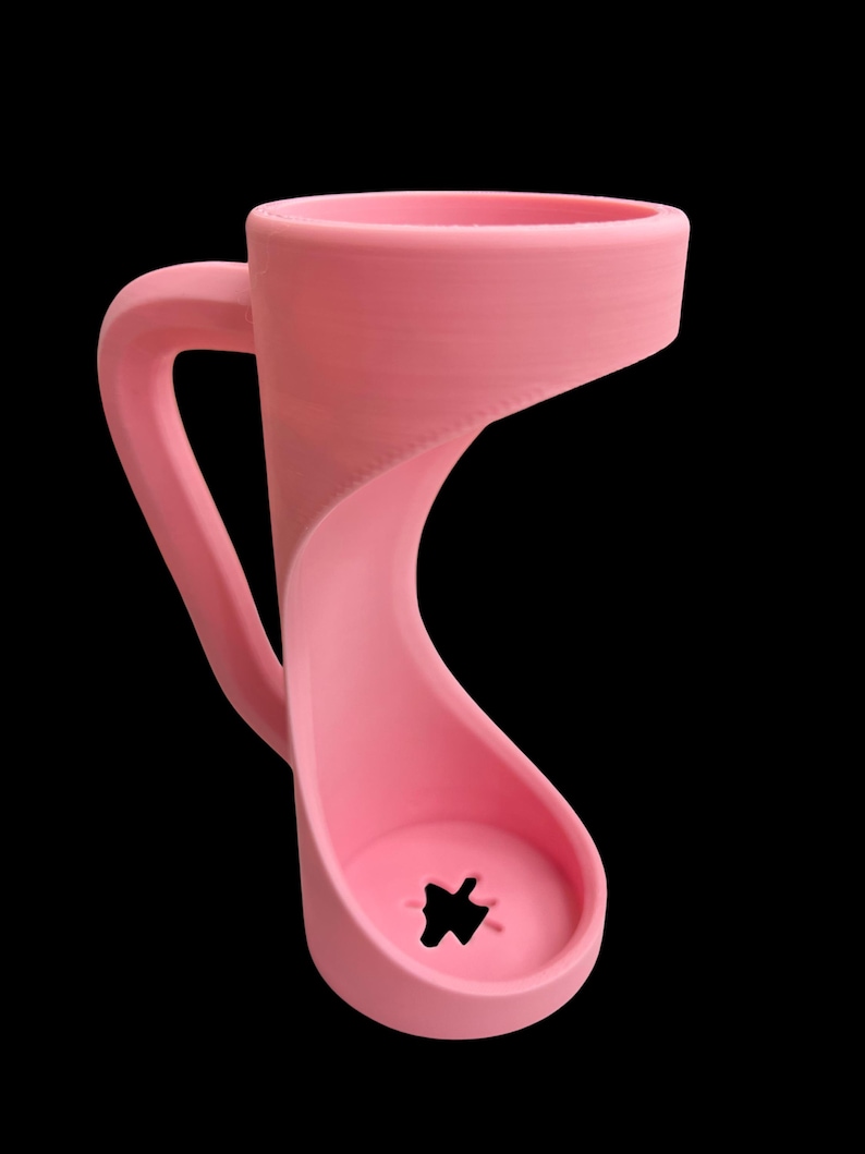 May include: A pink, uniquely shaped mug with a curved handle and a base with a star-shaped cutout. The mug's design features a continuous, flowing form, and it is set against a black background.