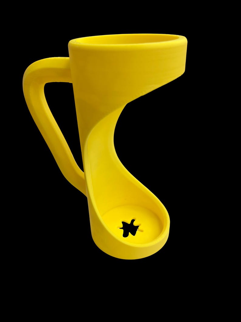 May include: A bright yellow, uniquely designed mug with a curved handle and a distinctive, open-bottomed base. The mug's form is a continuous, flowing shape, with a star-shaped hole at the base. The background is solid black.