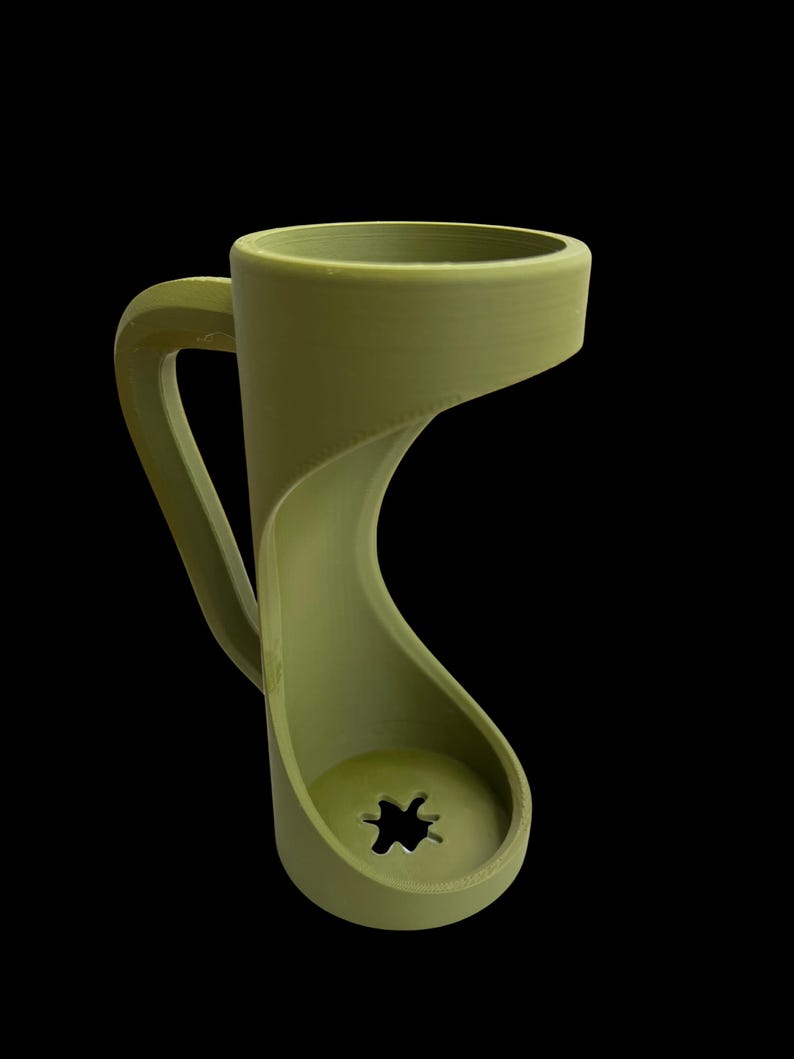 May include: A unique olive green mug with a distinctive, flowing design. The handle curves gracefully into the base, which features a star-shaped cutout. The mug's form is modern and sculptural, set against a black background.