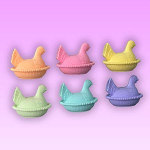 May include: Six colourful hen-shaped containers in orange, pink, yellow, green, blue, and purple. Each hen sits in a basket-like base. The background is a gradient of pink and purple.