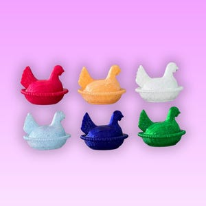 May include: Six brightly coloured hen ornaments in red, orange, white, light blue, dark blue, and green. Each hen sits in a matching nest. The background is a pink to purple gradient.
