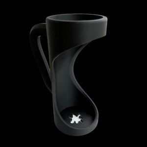 May include: A black coffee mug with a unique, open-sided design. The handle curves gracefully, and the base features a star-shaped cutout. The mug is made of a matte material and stands out against the black background.