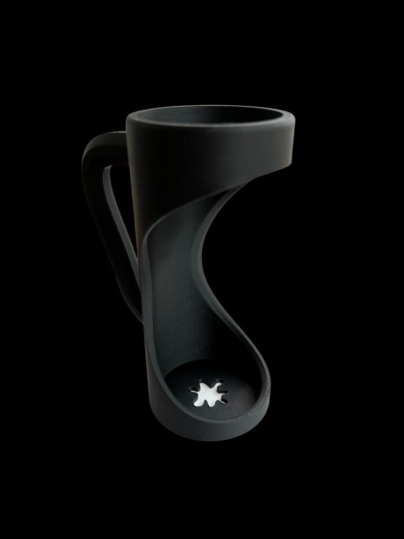 May include: A black coffee mug with a unique, open-sided design. The handle curves gracefully, and the base features a star-shaped cutout. The mug is made of a matte material and stands out against the black background.