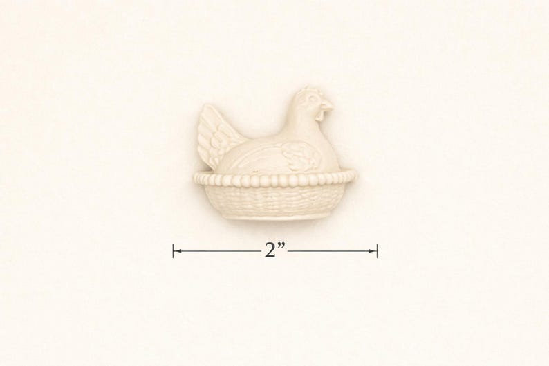 May include: A cream-coloured ceramic hen figurine, 5 cm in length, sitting in a woven basket. The hen has detailed feathers and a beak. The basket has a textured, woven design. The figurine is a decorative item.