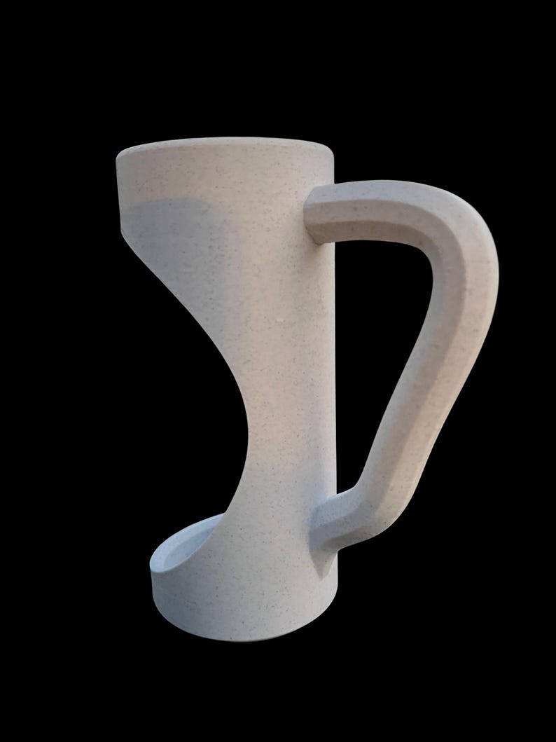 May include: A light gray, textured mug with a unique, curved handle. The mug has a wide, cylindrical body and a rounded base. The handle is thick and angular, extending from the side of the mug.