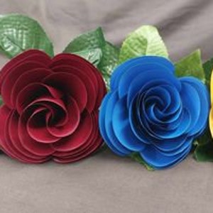 Puede incluir: Cuatro rosas de papel en diferentes colores: blanco, burdeos, azul y amarillo. Las rosas est&aacute;n dispuestas en fila y tienen un tallo verde.