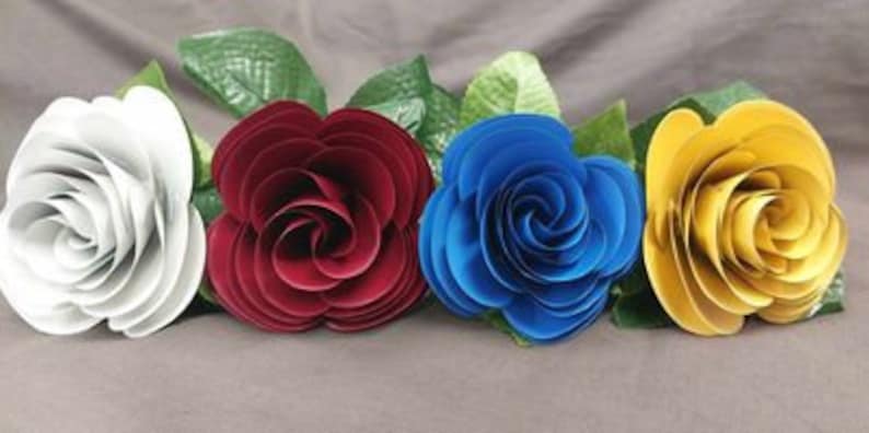 Puede incluir: Cuatro rosas de papel en diferentes colores: blanco, burdeos, azul y amarillo. Las rosas est&aacute;n dispuestas en fila y tienen un tallo verde.