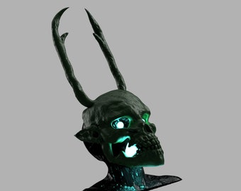 May include: A dark green skull sculpture with glowing green eyes and mouth. The skull has two long, curved horns extending upwards from the top. The sculpture has a textured surface and is set against a gray background.