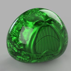 Può includere: Un oggetto lucido a forma di uovo verde con un volto stilizzato scolpito sulla sua superficie. Il volto ha un ampio sorriso dentato. L'oggetto ha il testo "Darryl Off Earth" e altro testo in basso. L'oggetto è su sfondo grigio.