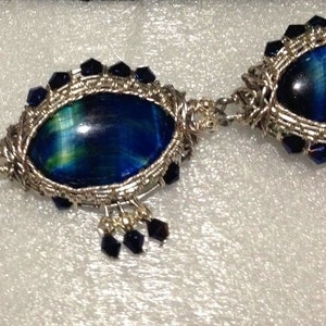 May include: A silver wire wrapped bracelet with three blue and green tiger's eye stones. The stones are oval shaped and set in silver wire with blue crystal accents.