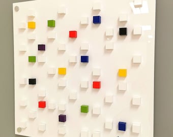 Puede incluir: Un lienzo cuadrado blanco con una cuadrícula de cuadrados pequeños, algunos de los cuales están pintados en varios colores, incluidos rojo, amarillo, azul, verde, negro y morado. El lienzo está firmado "Bernhardt" en la esquina inferior derecha.