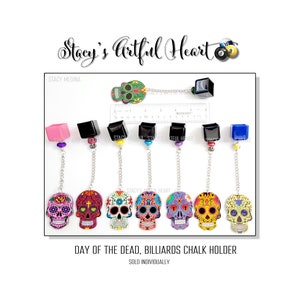 Puede incluir: Siete porta tizas de billar de colores con forma de calavera del Día de Muertos, con tapas de diferentes colores. Las tapas son rosa, negra, negra, negra, azul y negra. Las calaveras están decoradas con flores y otros diseños. El texto "Day of the Dead, Billiards Chalk Holder" y "Sold Individually" está impreso debajo de las calaveras.